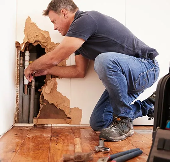 Plumber repairing a leaking pipe inside a damaged wall in Covina, CA
